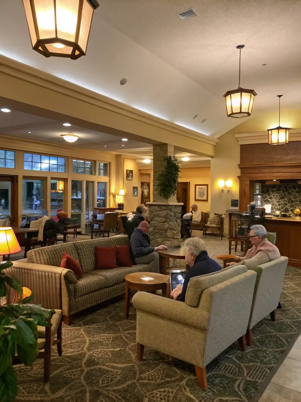 A warm, inviting photo of a modern community lounge with comfortable seating, people engaged in animated conversation, and informational posters about upcoming events, representing the welcoming meeting spaces at MJC.